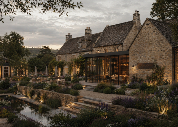 Stone manor with glass-walled dining room and warm outdoor lighting, surrounded by a manicured garden at dusk?