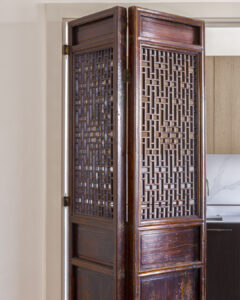 Pair of antique wooden folding doors with geometric lattice panels, opened to reveal a kitchen with light wood cabinetry behind.