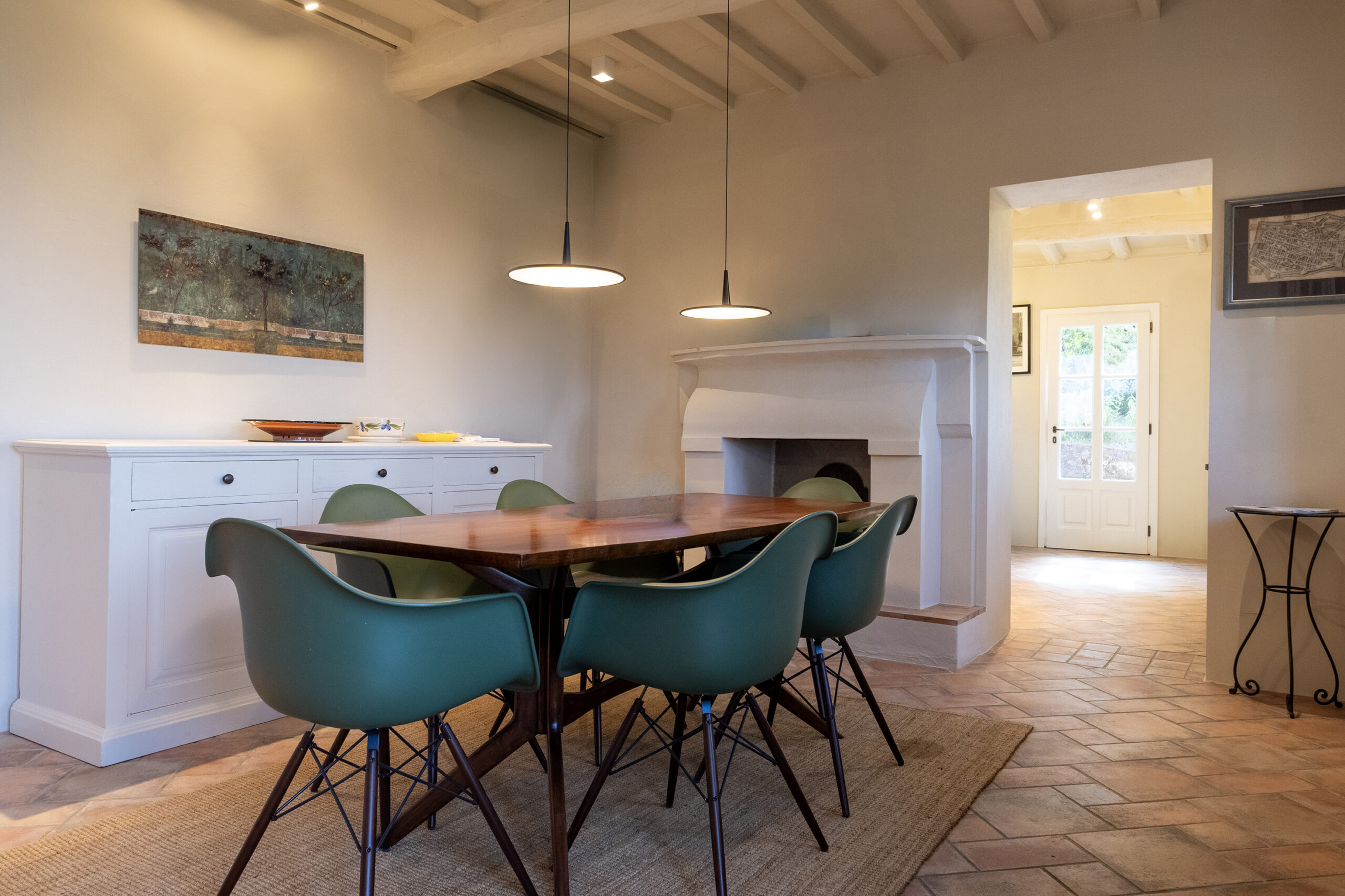 Dining room with a long wooden table and teal chairs, white sideboard, and two pendant lights overhead.