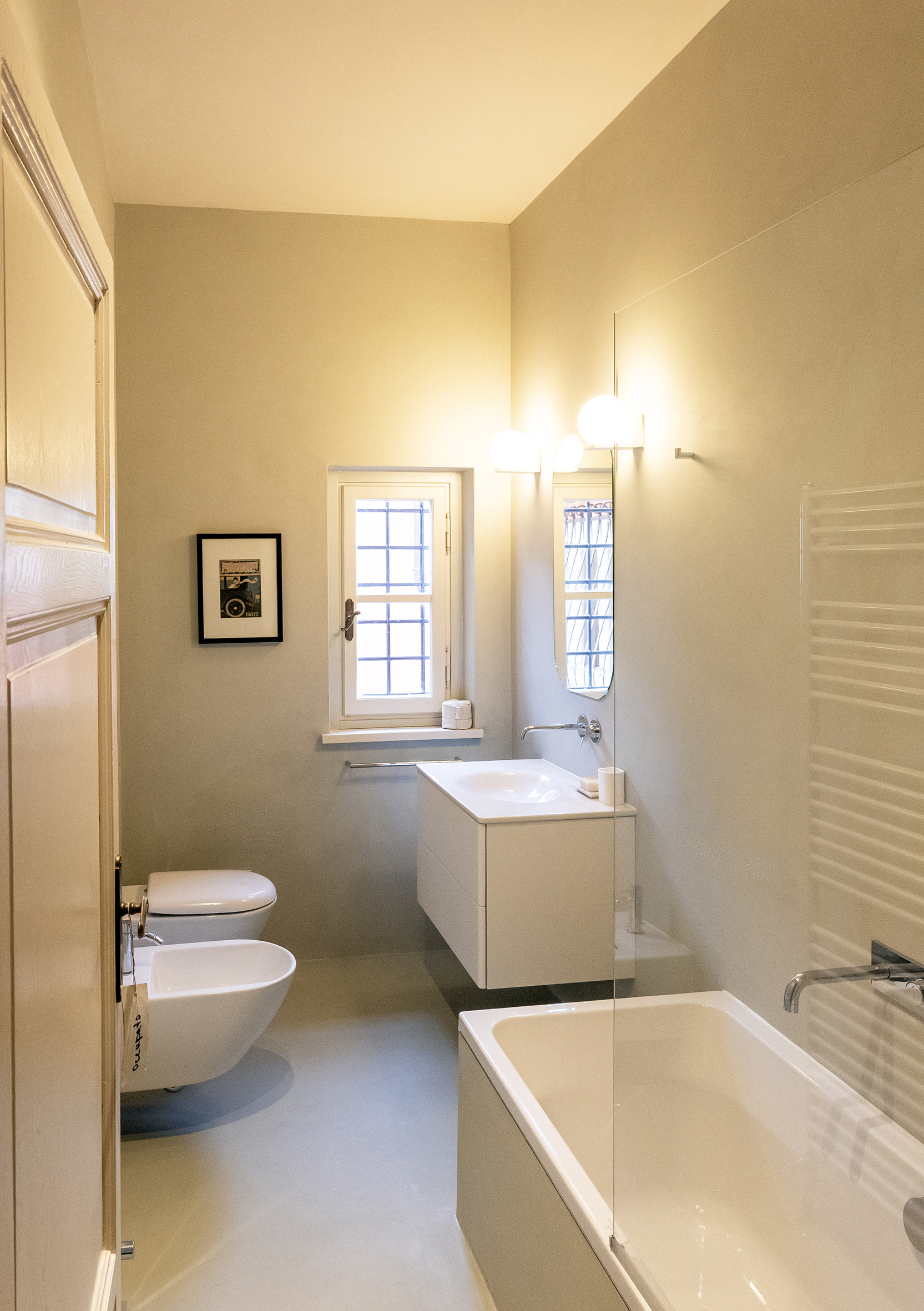 Modern bathroom with white vanity, mirror, and globe lights, bathtub along the right, and a toilet and bidet on the left wall.
