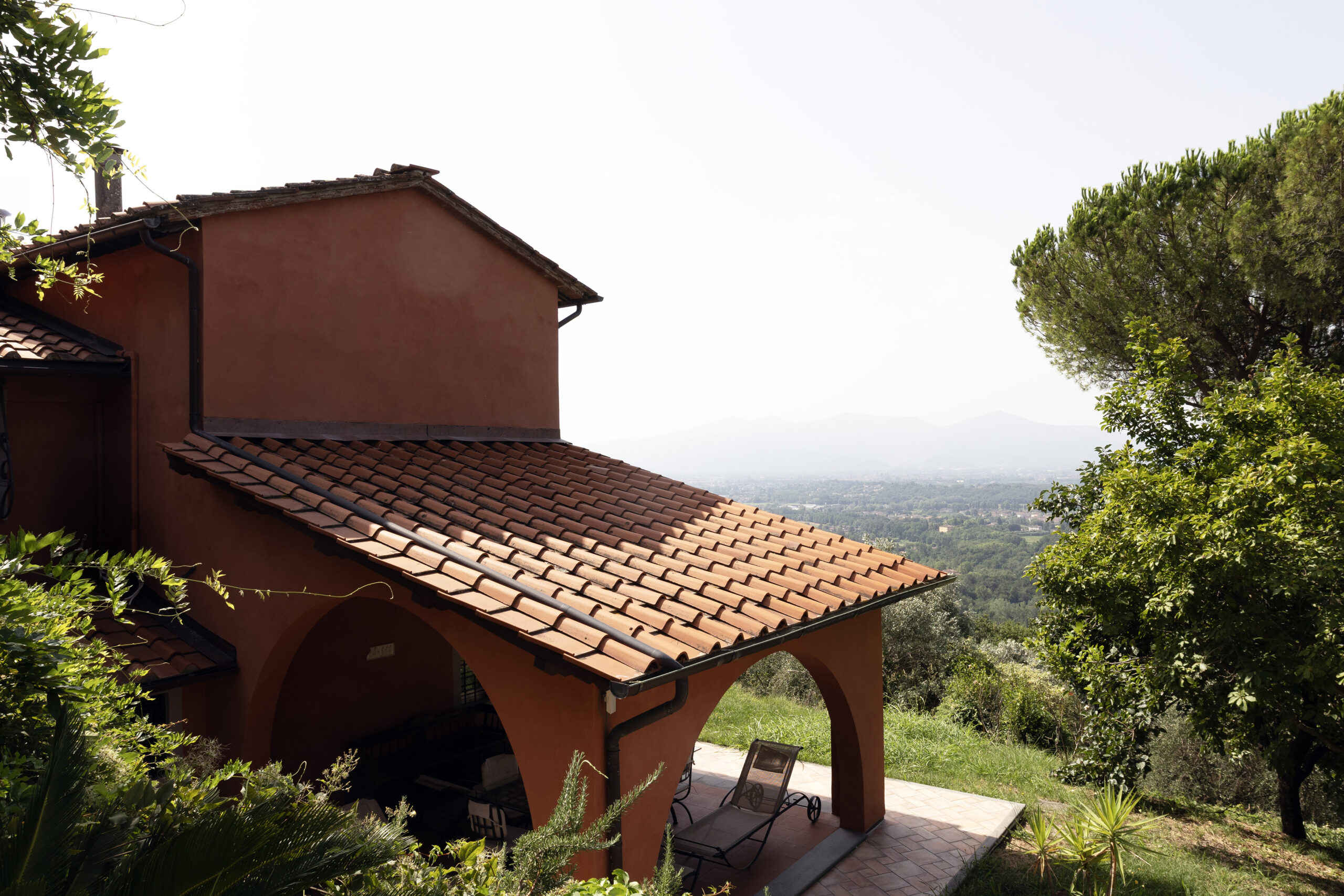 Terracotta-colored house with a red tile roof and arched patio, overlooking green hills and distant mountains in the distance.