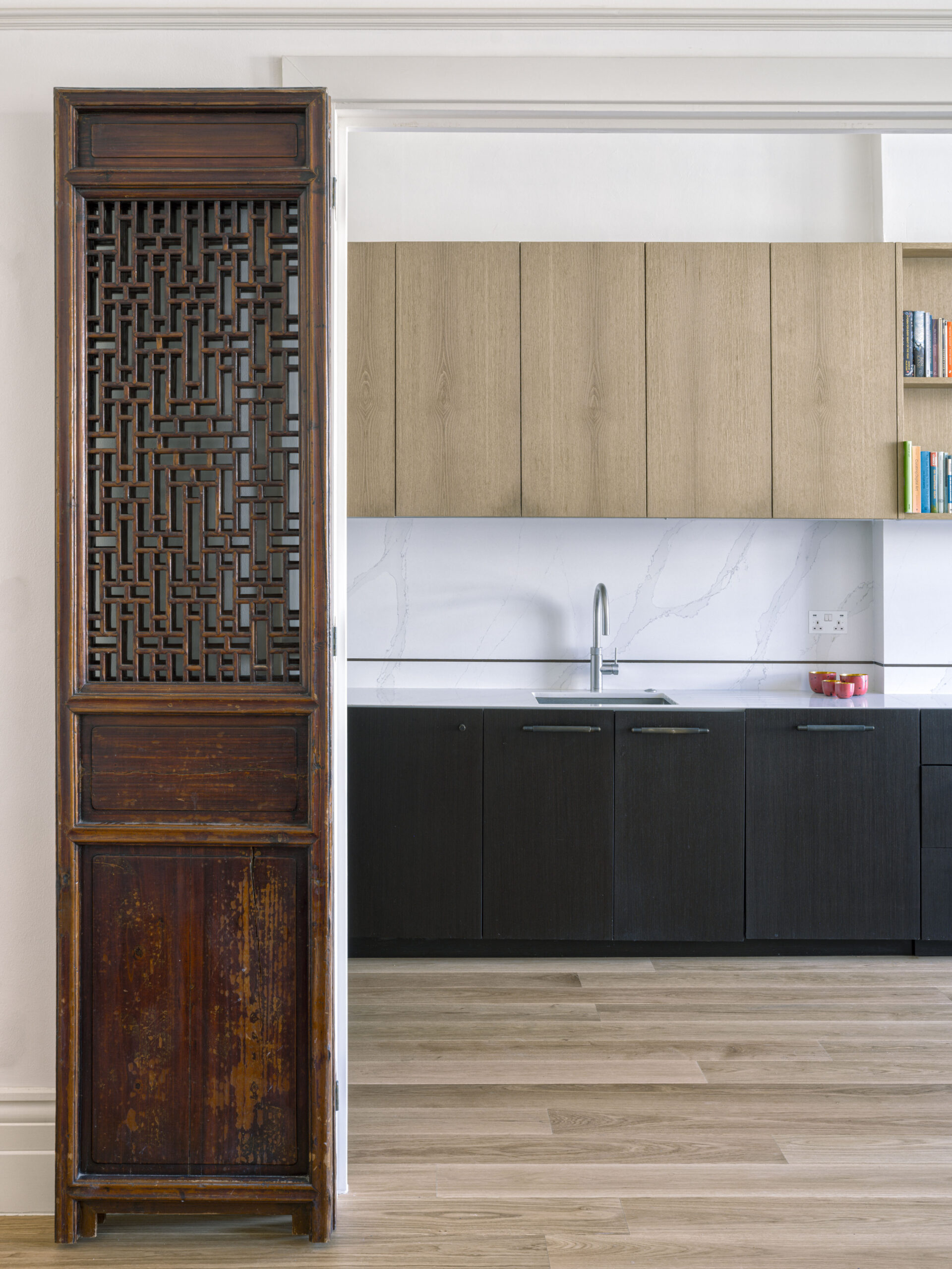 Ornate dark wood carved cabinet panel next to a modern kitchen with light wood upper cabinets and a marble backsplash.