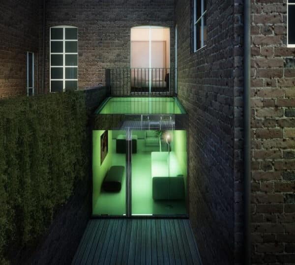 Green-lit glass-walled living space set in a brick courtyard, seen through sliding doors at night.